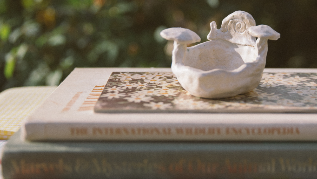Small white ceramic sculpture of a snail and mushrooms